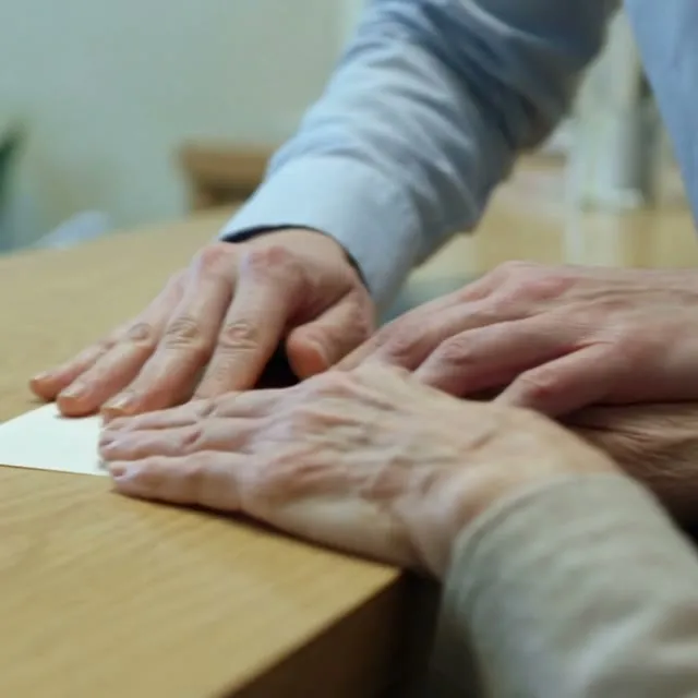 Una mano apoyada sobre la de otra persona, en un mostrador.